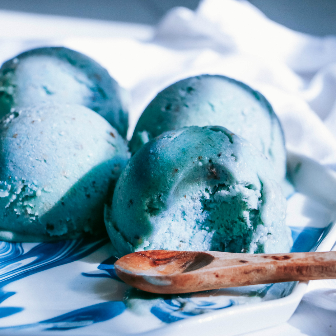 Delicious scoops of vibrant blue Mermaid Nicecream made with BlueMAJIK, served on a swirled blue and white dish with a wooden spoon, highlighting a colorful and nutrient-rich treat.