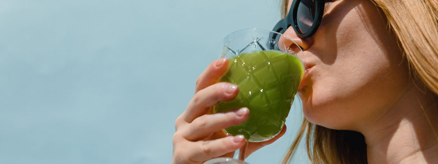 Close-up of a person enjoying a refreshing green drink under a bright blue sky. The image conveys a sense of health, vitality, and well-being.