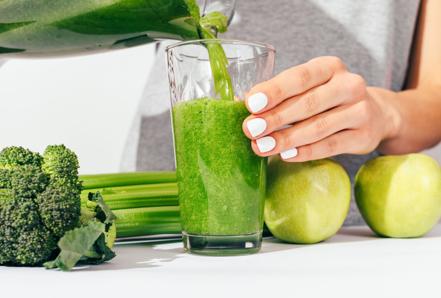 Pouring a vibrant green superfood smoothie into a glass with fresh broccoli, celery, and green apples, highlighting the nutrient-rich benefits of E3AFA/E3Live for upgrading your daily greens.